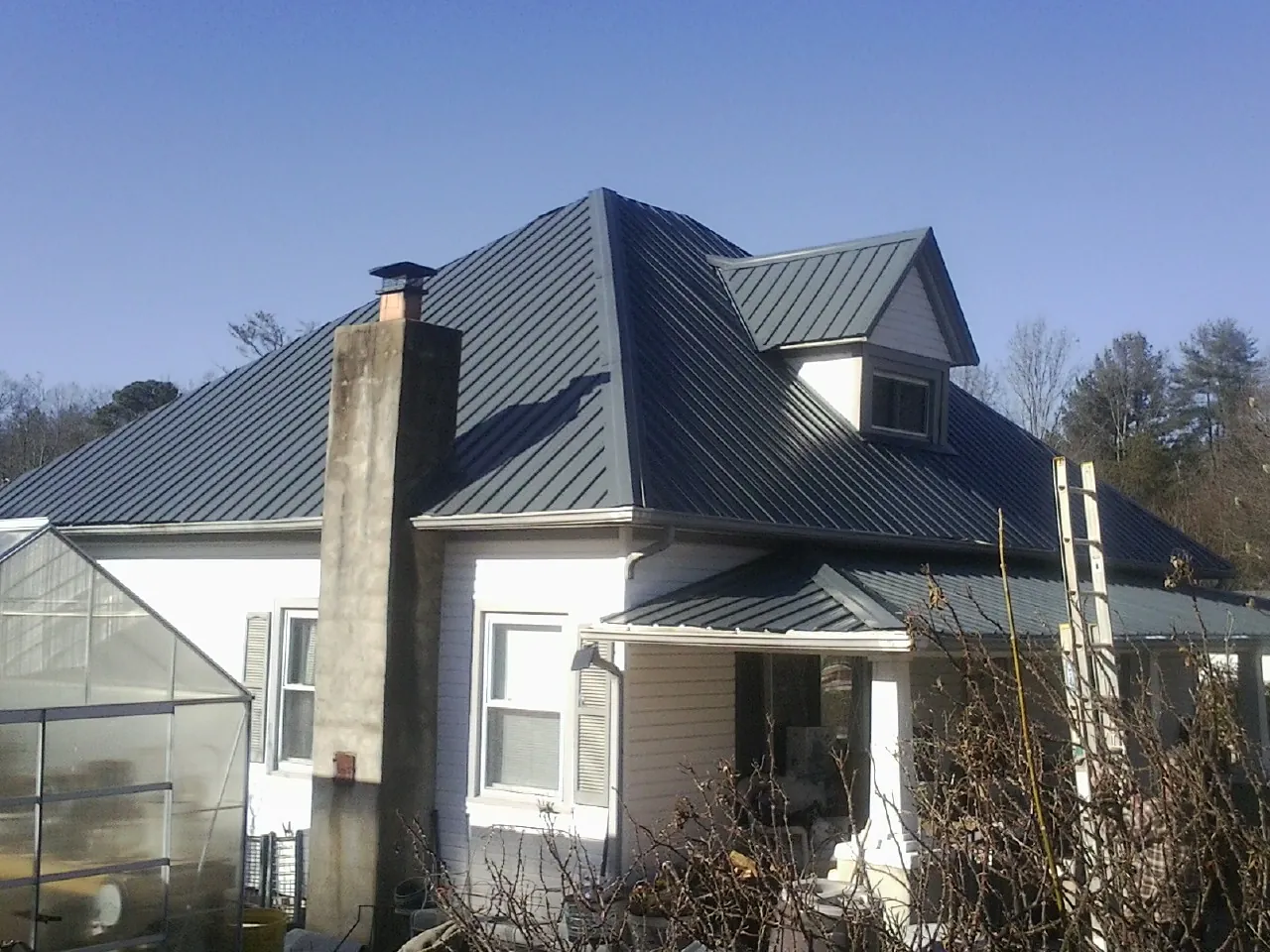 Dark blue standing seam metal roof on a white farmhouse with dormer — Slate & Tile Roof Repair by Roofing Brothers in Delavan