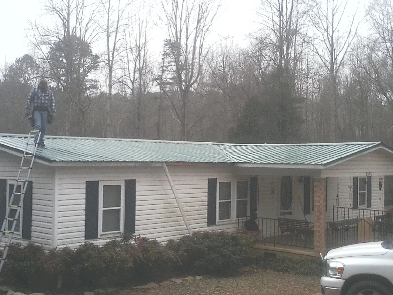 Worker on a ladder beside a new green metal roof on a ranch home in Delavan