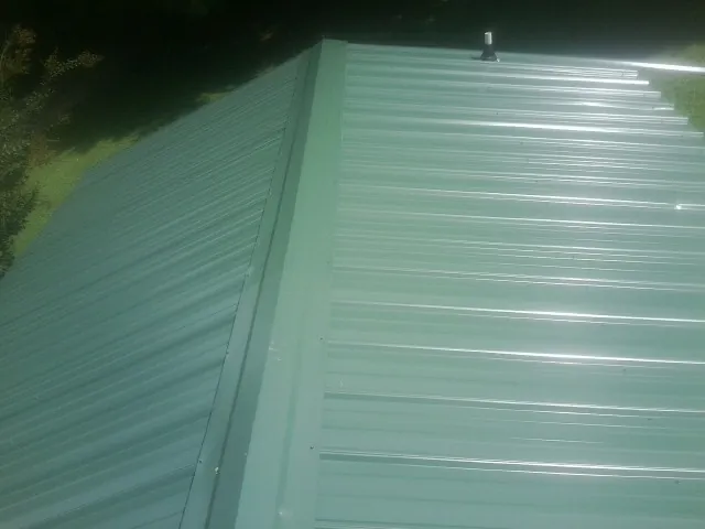 New green metal panels meeting at the ridge of a roof — Flat Roof Repair work by our crew in Delavan