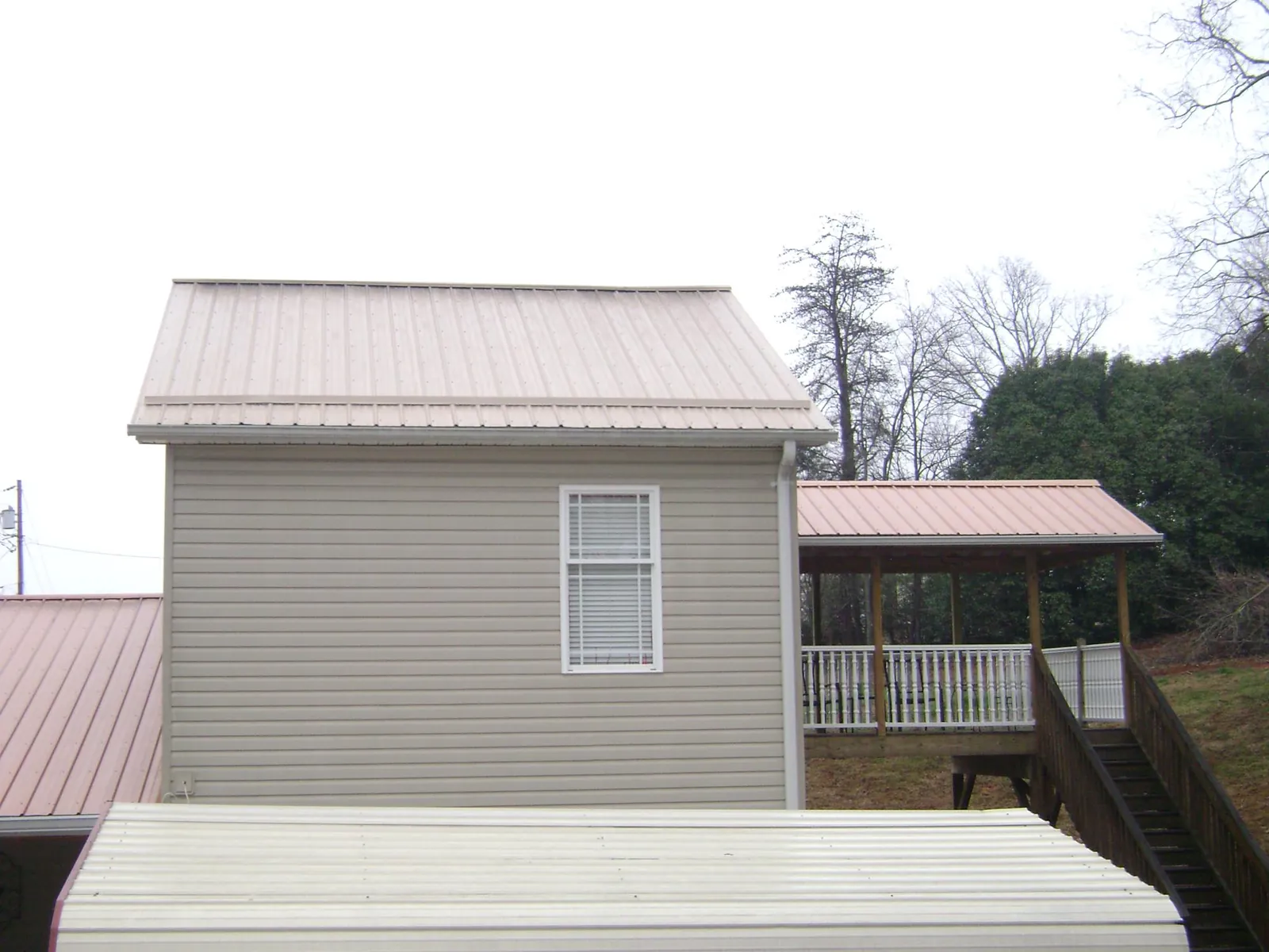 Tan metal roofs on a two story addition and attached porch, from a Roof Replacement job in Delavan
